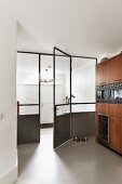 Wooden kitchen cupboards with fitted appliances next to glass and metal door element
