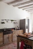 Blick über Theke auf Küchenzeile, mit Massivholzunterschränken, seitlich moderner Kühlschrank aus Edelstahl