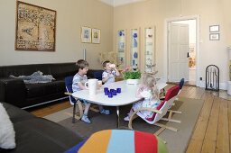 Kinder am niedrigen Esstisch im Wohnzimmer mit schwarzen Ledersofas