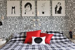 Schlafzimmer mit schwarz-weissen Zeichnungen, floralem Paisleymuster und karierter Bettwäsche, Farbakzent mit roten Kissen