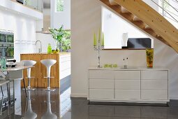 Sideboard under staircase; kitchen island with bar stools to one side