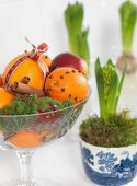 Orange and clove pomanders and cinnamon sticks in glass bowl next to potted hyacinths