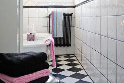 View of free-standing bathtub and colour-coordinated towels in black and white tiled bathroom