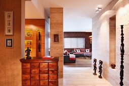 Apothecary cabinet in hallway, ethnic sculptures on floor against wall and view into lounge area in background