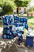 A crocheted blue blanket and cushion cover with a floral pattern on an antique bench in a garden