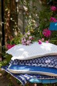 A stack of cushions with various blue and white covers and phlox flowers on a chair in a garden
