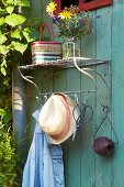 A vintage exterior coat rack with a bunch of flowers on a shelf with a sun hat and garden utensils on hooks