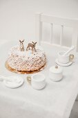 Nut cake decorated with icing sugar and animal figurines on child's table with dolls' tea set