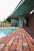 Brick-paved edge of pool below curved concrete roof in classical modernist style