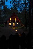Romantische Abendstimmung mit beleuchtetem Holzhaus auf Waldlichtung und Bodenlaternen entlang des Gartenweges