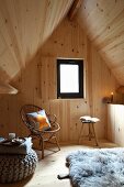 Holzverkleideter Rückzugsort unter Satteldach, Rattanstuhl mit Kissen und gemütlicher Sitzpouf auf Holzboden mit Schaffell