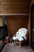 Gemütlicher Rattanstuhl mit hellem Schaffell auf Balkon, seitlich auf Holzboden Windlichter und Laternen
