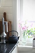 Zarte Blüten und Grünpflanze am Fenster, daneben Zitruspresse und Teekanne auf Küchenarbeitsplatte