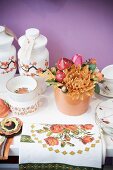 Blumengesteck mit Deko in Keramiktopf, zwischen Vasen und Geschirr auf Ablage