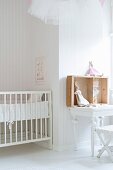 White-painted cot and rabbit soft toys on table in nursery with pale, striped wallpaper