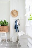 White-painted wooden bench, straw hat on coat peg and potted plant in vintage wooden crate