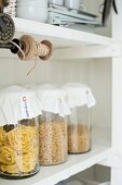 Pasta in storage jars with decorated lids and vintage thread reel on white kitchen shelves