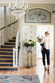 Foyer with white and blue wallpaper, curved staircase, bouquet and woman carrying baby