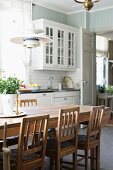Wooden chairs around dining table in country-house kitchen with white cupboards