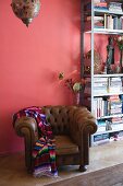 Eclectic ambiance with traditional leather armchair and ethnic blanket in front of metal bookcase against pink wall
