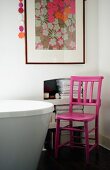 Pink-painted wooden chair next to partially visible modern bathtub and framed floral picture on wall