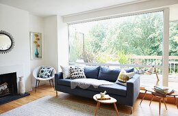 Grey couch and small, wooden fifties side table in front of glass wall
