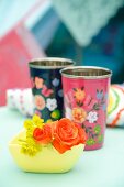 Orange roses in yellow bowl in front of floral beakers