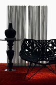 Plastic shell chair with perforated floral pattern and vase on pedestal tale on orange, long-pile rug