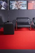 Lounge Sessel, Sitzhocker und Rückwand in dunklem Grau, belebt durch roten Teppich und Bildergalerie