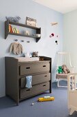 Changing table painted grey brown below matching shelves on wall painted pale blue and white rocking chair in corner to one side