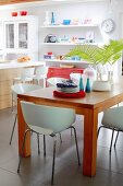 White shell chairs around wooden table in front of modern kitchen counter with bar stools and floating shelves