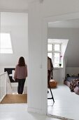 Woman walking down bright staircase and view into bedroom with sloping ceiling