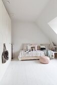 Rosa Sitzpouf auf weissen Dielenboden vor romantisch gestaltetem Bett mit Kissen und Tagesdecke