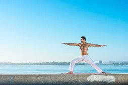 A young man by the sea wearing white yoga trousers