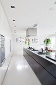 Long, free-standing kitchen counter with black base units in designer kitchen with recessed spotlights in suspended ceiling