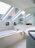 Bathtub with marble surround below row of skylights; mirrored wall with niche in background