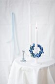 Small forget-me-not wreath draped over white candle in candlestick