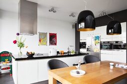 Esstisch mit schwarzen Pendelleuchten in offener weißer Küche mit freistehender Theke und Einbaugeräten