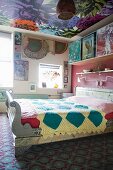 Colourful bedroom in mixture of patterns: ornate rug, floral wallpaper on ceiling and patterned quilt on bed