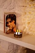 Box of matches with portrait of woman on lid and tealight in brass crown-shaped holder in front of stacked candles