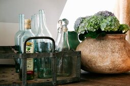 Glass bottles in metal bottle carrier next to ceramic vase of hydrangea flowers