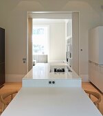 Esstisch und Küchentheke Kombination in Weiß, im Hintergrund Durchgang mit Blick ins Wohnzimmer