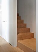 Blick vom Gang auf moderne Holztreppe in schmalem Treppenhaus