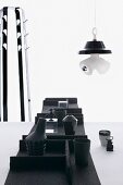 Black containers in felt trays on table, lamp sculpture and coat stand in background