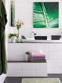 White-tiled bathroom with towels on step leading to whirlpool tub below picture with leaf motif