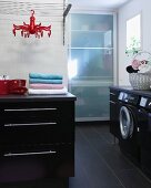 Moderner Waschraum mit schwarzen Unterschränken und integrierter Waschmaschine, im Hintergrund Schrank mit Glas Schiebetür