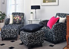 Armchairs and matching ottomans with ornate black pattern on grey upholstery in lounge area