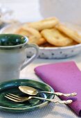 Vintage cutlery on green ceramic plates with dish of pastries in background