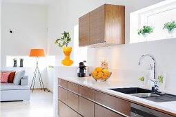 Offene Küche in Holzausführung mit weisser Arbeitsplatte, im Hintergrund Stehleuchte mit orangefarbenem Schirm in Loungebereich