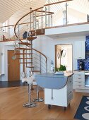 Scandinavian kitchen with island counter on castors in open-plan interior; steel and wood spiral staircase leading to upper storey